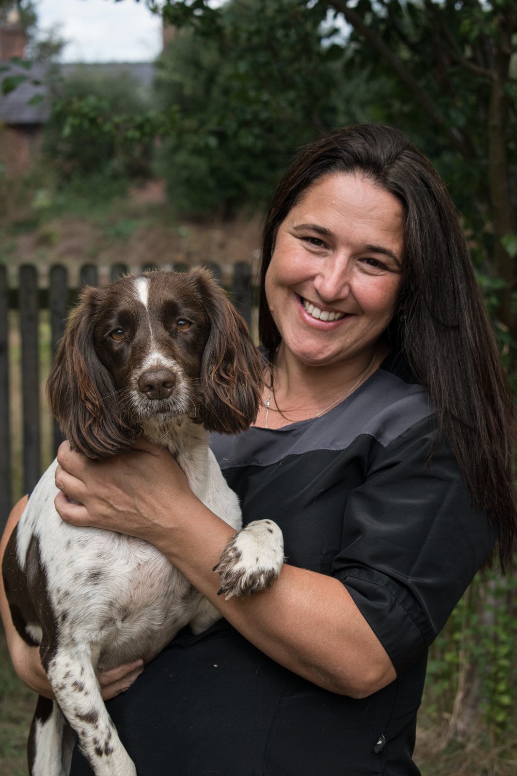 Eda holding a springer spaniel outside, smiling towards the camera